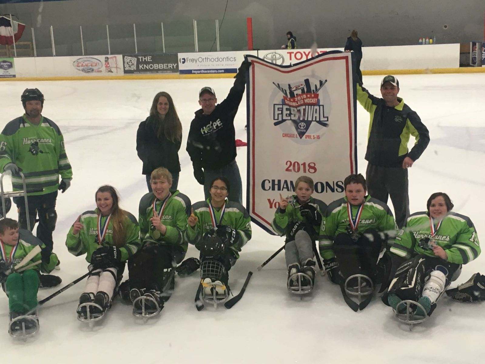 Group of sled hockey athletes smiling at camera holding up pointer finger